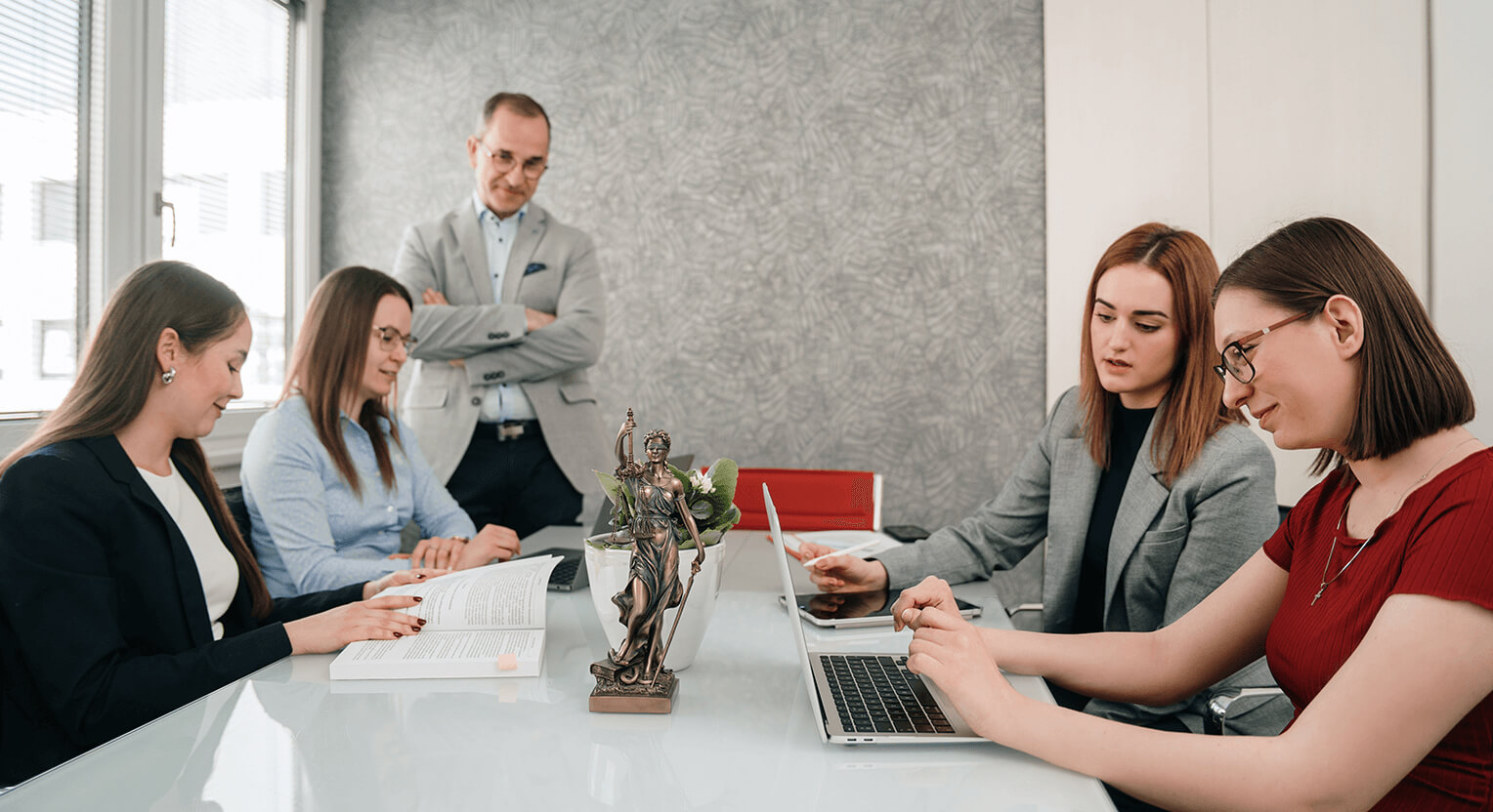 A képen egy ügyvéd csapat látható, amint egy értekezleten egyeztetnek a cégjog, jogi megfelelőség (compliance) és szerződések terén. A csapat tagjai közösen dolgoznak azon, hogy ügyfeleik számára a legmegfelelőbb jogi megoldásokat találják meg. Az asztalon szerződések és egyéb jogi dokumentumok láthatók, mindenki figyelmesen hozzájárul a beszélgetéshez, hogy biztosítsák a pontos és átgondolt jogi döntéseket.